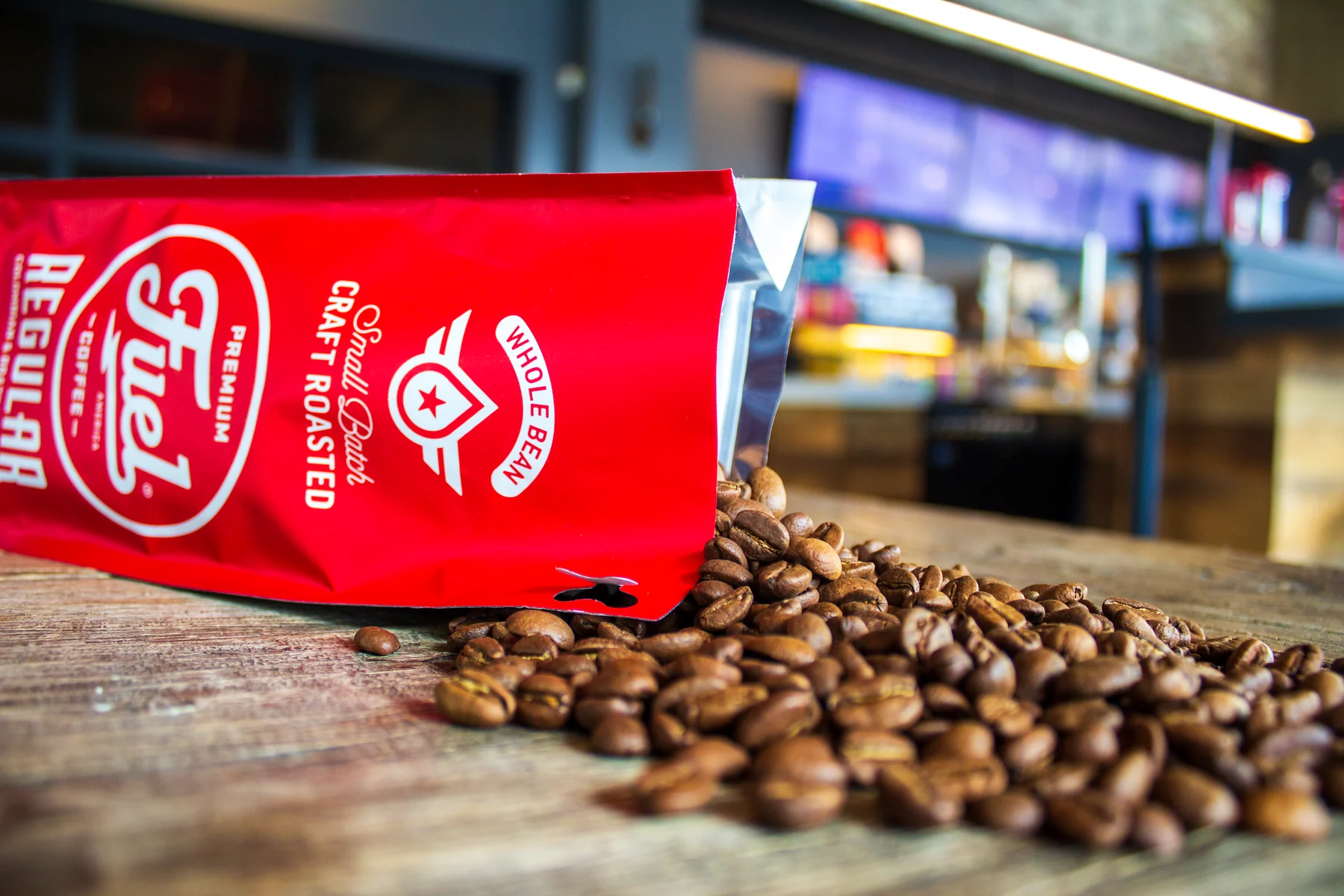 Fuel America whole-bean coffee spilling from a red bag onto a café table