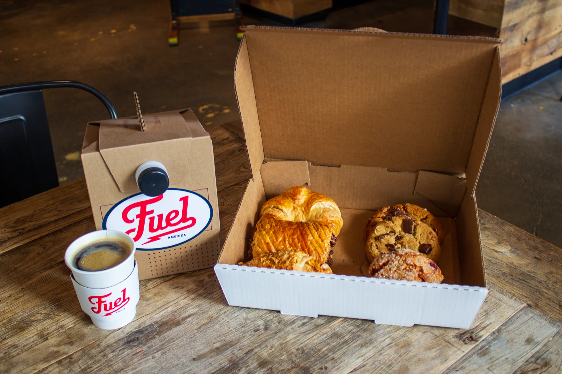 Fuel America coffee carrier and cup beside an open box of assorted pastries.